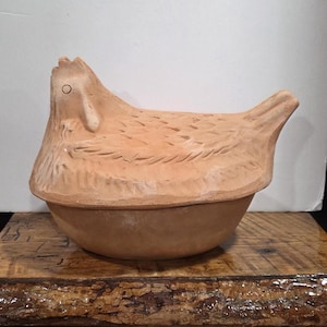 May include: A terracotta chicken-shaped casserole dish. The lid is shaped like a chicken with detailed feather and head features. The base is a rounded bowl. The dish is a warm, earthy tone, ideal for kitchen decor or serving.
