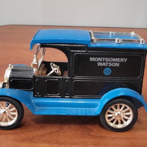 May include: A die-cast model of a vintage delivery truck. The truck is black with blue fenders, roof, and accents. The words "MONTGOMERY WATSON" are printed on the side. The wheels are silver and the truck has a detailed interior.