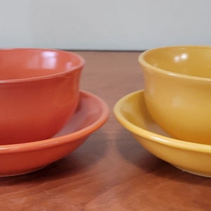 Puede incluir: Dos juegos de tazas de té y platillos. Un juego es naranja y el otro es amarillo.