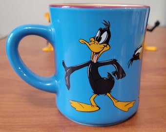 1998 Warner Brothers Studio Daffy Duck Coffee Mug and Four Plastic Daffy Duck Figurines in Different Poses
