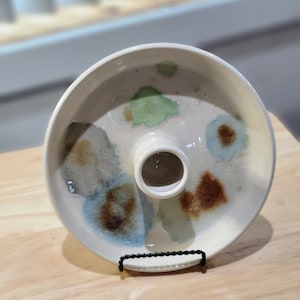 May include: White ceramic serving dish with a central stand and a ring of brown, blue, and green watercolor-like designs.