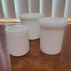 以下が含まれることがあります： さまざまなサイズの白いセラミック製の容器が3つあります。容器は円筒形で、滑らかで光沢のある仕上げになっています。