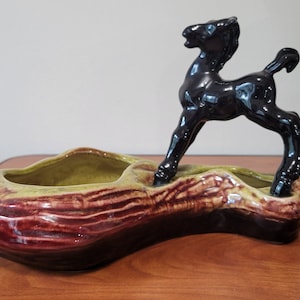 以下が含まれることがあります： 黒い馬の置物が乗った、丸太の形をしたセラミック製のプランター。プランターは緑と茶色で光沢のある仕上げです。