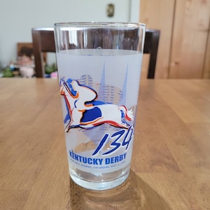 Puede incluir: Un vaso transparente con un diseño esmerilado que presenta un caballo, el número 134 y las palabras "Kentucky Derby". El vaso también incluye el texto "Churchill Downs, Saturday, May 3, 2008".