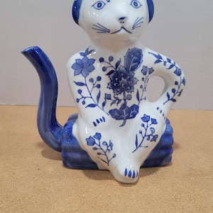 May include: A blue and white porcelain teapot shaped like a sitting cat with a floral design. The teapot has a lid and a spout.