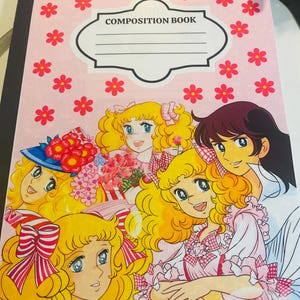 May include: A composition book with a pink cover adorned with red flower illustrations. The cover features a cartoon illustration of several girls with blonde hair and blue eyes. The words "COMPOSITION BOOK" are printed on the cover.
