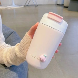May include: A pink and white insulated travel mug with a cloud-shaped design and the text "Thank You".