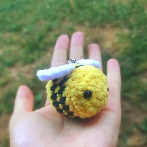 Peut inclure: Un porte-clés en forme d'abeille crocheté avec un corps rayé jaune et noir, des ailes blanches et des yeux noirs.