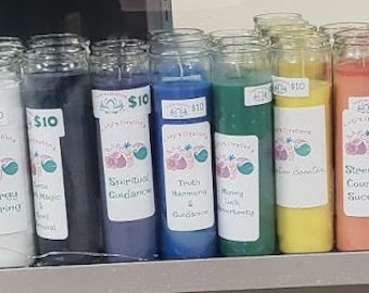 May include: A collection of colorful pillar candles in glass jars. Each candle is a different color, including red, white, blue, green, yellow, and orange. Labels on the candles include text such as "Chakra Healing" and "Spiritual Guidance".