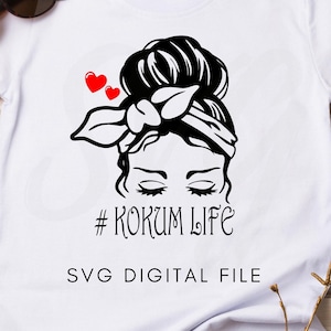 Può includere: Maglietta bianca con un'illustrazione in bianco e nero di una donna con un chignon disordinato e una fascia per capelli. Il testo "#KOKUM LIFE" e "SVG DIGITAL FILE" sono stampati sotto l'illustrazione.