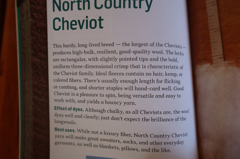 Peut inclure: Page de livre ouverte avec du texte sur la laine North Country Cheviot. Le texte d&eacute;crit les caract&eacute;ristiques de la laine, notamment son volume &eacute;lev&eacute; et sa r&eacute;silience. Il mentionne &eacute;galement les utilisations de la laine pour les pulls, les chaussettes et autres v&ecirc;tements.