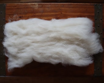 May include: A large clump of white wool fibers on a wooden surface.