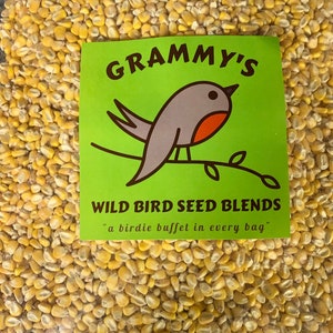 May include: A close-up of a bag of yellow wild bird seed with a green and white label that says "Grammy's Wild Bird Seed Blends" and "a birdie buffet in every bag".