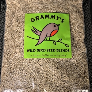 May include: A clear plastic bag filled with wild bird seed. The bag has a green and white label with the text "GRAMMY'S WILD BIRD SEED BLENDS" and a cartoon robin on a branch. The text below the robin says "a birdie buffet in every bag."