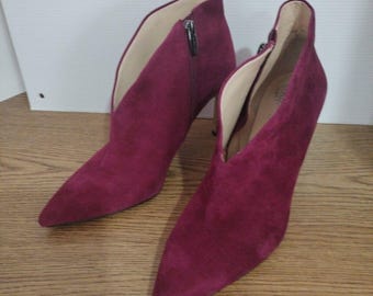 May include: A pair of burgundy suede ankle boots with a pointed toe and a stiletto heel. The boots have a side zipper and a cut-out detail on the front.