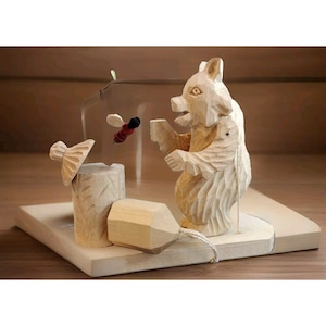 May include: A wooden bear figurine with a carved face and a bee figurine flying towards it. The bear is standing on a wooden base with a small wooden beehive.