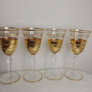 Puede incluir: Juego de cuatro copas de vino de vidrio transparente con ribete dorado. Las copas tienen una copa ancha y un tallo alto.