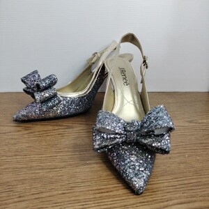 May include: A pair of silver glitter slingback heels with a bow on the toe. The heels are labeled "J.Renee".