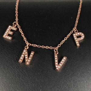 May include: A rose gold necklace with a chain and four charms, each charm is a letter with clear rhinestones. The letters are E, N, V, and P.