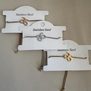 May include: Three stainless steel bracelets with a small infinity symbol charm. The bracelets are on white cards with the text "Stainless Steel" printed on them.