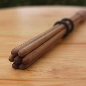 Peut inclure: Un ensemble de chevilles en bois, maintenues ensemble par un élastique noir. Les chevilles sont de couleur marron chaud, avec des extrémités arrondies. Le fond est une surface en bois brun clair.