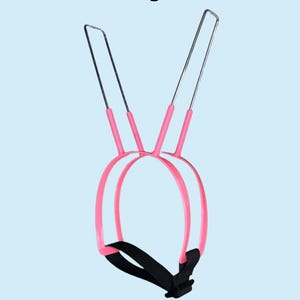 May include: A Doberman Pinscher ear posting brace featuring a pink plastic frame with two vertical metal rods and a black adjustable strap. The text Doberman Pinscher Ear Posting Brace and Post ears in under 60 seconds is printed on the image.