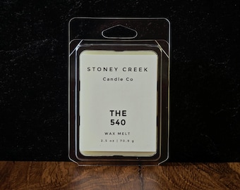 May include: A rectangular clear plastic clamshell package containing a cream-colored wax melt. The white label features black text reading STONEY CREEK Candle Co, THE 540, WAX MELT, and 2.5 oz | 70.9 g. The packaging has a top hole for hanging.