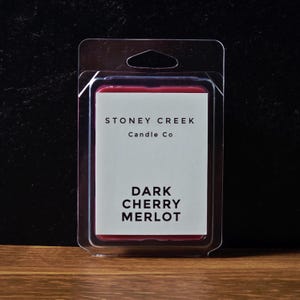 May include: A rectangular wax melt package with a dark red wax and a white label. The label reads "STONEY CREEK Candle Co" and "DARK CHERRY MERLOT". The package is in a clear plastic clamshell.