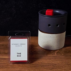 May include: A black and speckled ceramic wax warmer with a red wax cube on top. Next to it is a package of wax melts with the text "Stoney Creek Candle Co" and "THE 540" on the label.