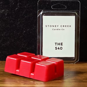 May include: A red wax melt with six cubes is displayed next to a clear plastic package. The package contains a white label with the text "STONEY CREEK Candle Co" and "THE 540". The wax melt is on a wooden surface.