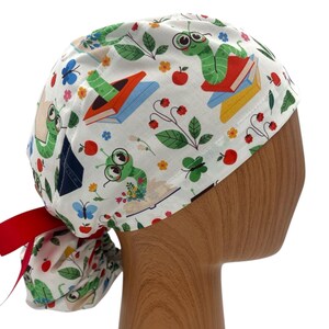 May include: A white scrub cap with a whimsical print featuring green cartoon caterpillars, books, red apples, and blue butterflies. The cap has a red ribbon tie at the back. The design is a playful and colorful theme.