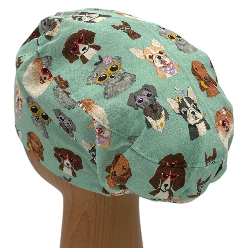 K&ouml;nnte beinhalten: Eine gr&uuml;ne OP-M&uuml;tze mit einem Muster aus Hunden, die Sonnenbrillen tragen. Die Hunde sind verschiedener Rassen und Farben, und einige tragen H&uuml;te oder Bandanas.