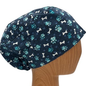 May include: A blue scrub hat with a pattern of paw prints and bones. The hat is made of a soft, comfortable fabric and is perfect for anyone who loves animals.