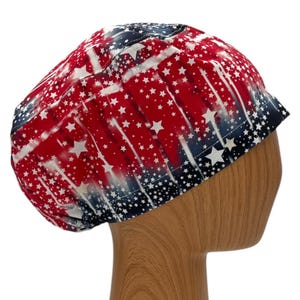 May include: A red, white, and blue patterned hat with a star design. The hat is made of fabric and has a rounded shape. The hat is displayed on a wooden head form.