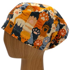 May include: A colorful scrub hat with a pattern of orange, black, and white cat paws and tails.