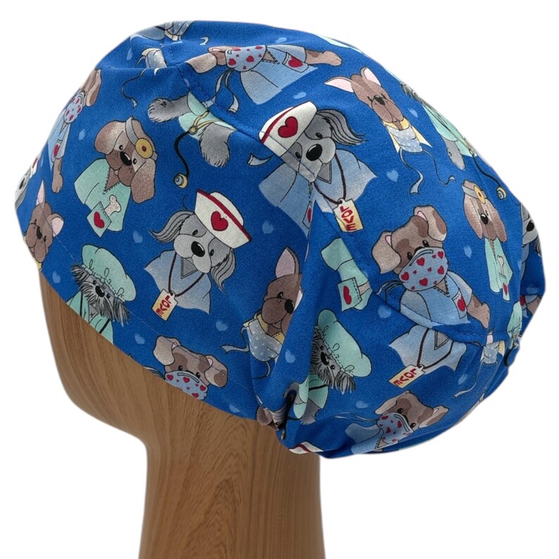 May include: Blue scrub hat with a pattern of cartoon dogs wearing nurse outfits and holding hearts. The dogs are wearing stethoscopes and have the words "Love" and "Doctr" on their collars.