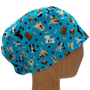 K&ouml;nnte beinhalten: Eine blaue OP-M&uuml;tze mit einem Muster aus Hunden und Knochen. Die M&uuml;tze befindet sich auf einem h&ouml;lzernen Mannequin-Kopf.