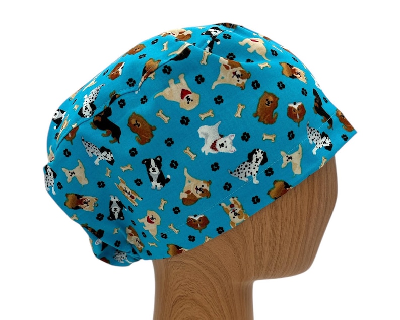 K&ouml;nnte beinhalten: Eine blaue OP-M&uuml;tze mit einem Muster aus Hunden und Knochen. Die M&uuml;tze befindet sich auf einem h&ouml;lzernen Mannequin-Kopf.