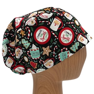 May include: A black scrub hat with a Christmas-themed print featuring cookies, candy canes, cocoa mugs, and Santa Claus. The text on the hat reads "Cookies for Santa".