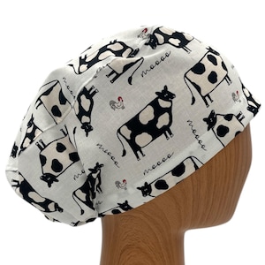 May include: White scrub hat with a black and white cow print and the word "moo" repeated throughout.