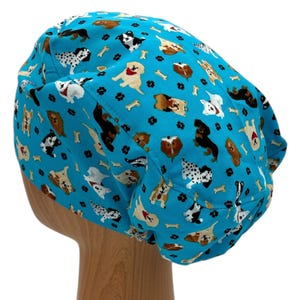 K&ouml;nnte beinhalten: Eine t&uuml;rkisblaue OP-M&uuml;tze mit einem Muster aus verschiedenen Hunderassen und Knochenmotiven.
