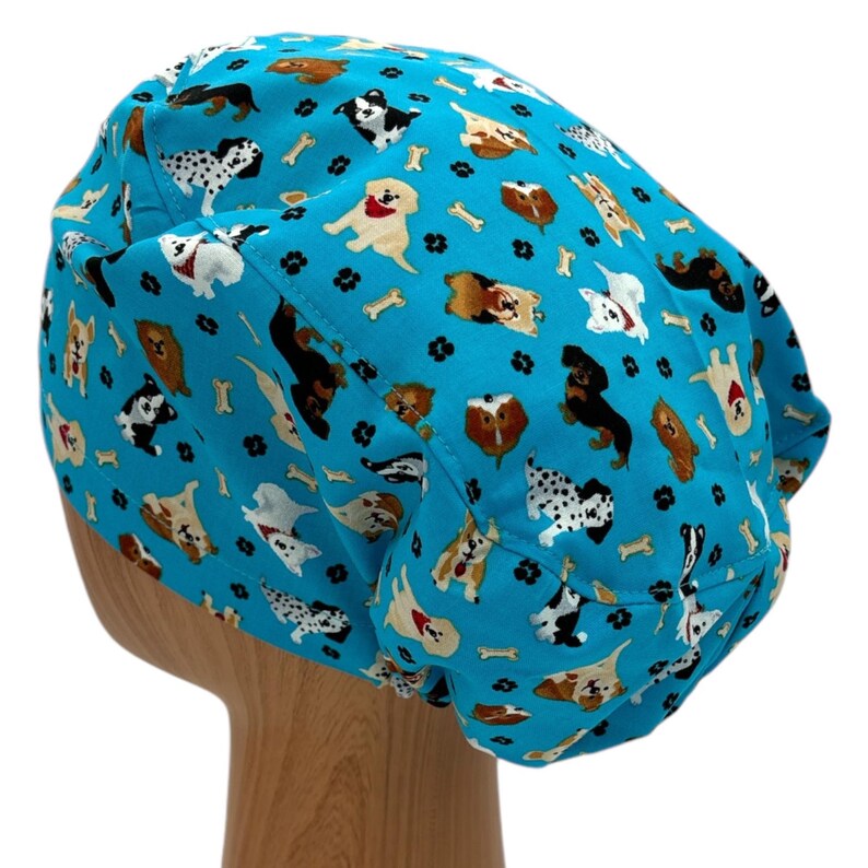 K&ouml;nnte beinhalten: Eine t&uuml;rkisblaue OP-M&uuml;tze mit einem Muster aus verschiedenen Hunderassen und Knochenmotiven.