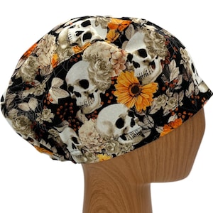 May include: Black scrub hat with a skull and floral print. The hat features white skulls, orange flowers, and black leaves on a black background.