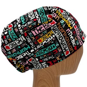 May include: Black scrub hat with a colorful print of the words "The Big Apple", "Manhattan", and "New York" repeated in various sizes and colors.