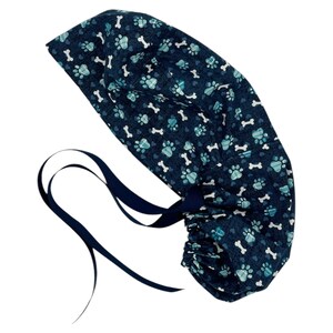 May include: A blue and white patterned surgical scrub cap with a tie closure. The pattern features paw prints and bones.