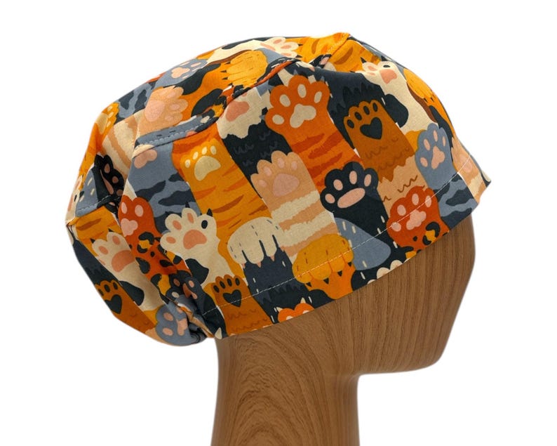May include: A colorful scrub hat with a pattern of orange, black, and white cat paws. The hat is made of a soft, comfortable fabric and is perfect for nurses, doctors, and other healthcare professionals.