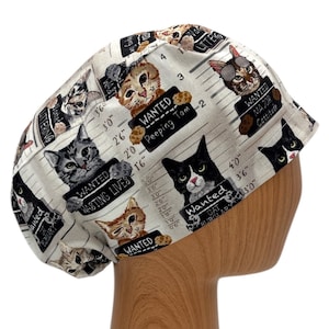 Beige scrub cap with a playful cat mugshot design, featuring whimsical illustrations of cats with humorous 'crime' labels like 'Peeping Tom' and 'Cat Burglar.'