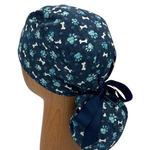 May include: A blue surgical scrub hat with a paw print and bone pattern. The hat has a blue ribbon tie.