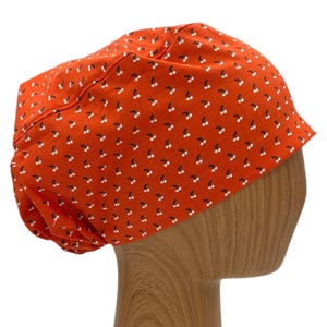 May include: Orange scrub hat with a white cherry print. The hat is made of a soft, comfortable fabric and is designed to be worn by medical professionals.