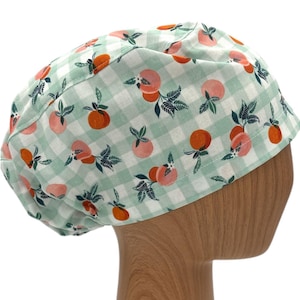 May include: A green and white gingham scrub hat with a peach and leaf pattern.